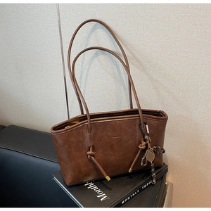 Detail view of deep brown faux leather tote bag with knot design and tennis charm