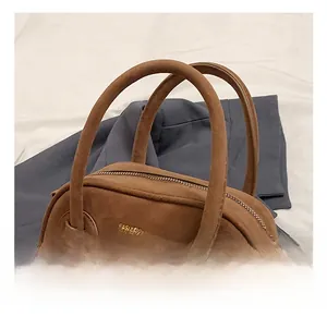 Gros plan du sac Boston en daim marron avec poignées rondes et texte doré élégant