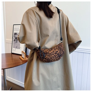Close-up of leopard print crescent bag with black strap worn by a model in a minimalist room