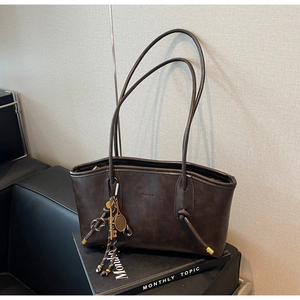 Detail of dark brown leather tote bag with vintage texture and metal tennis racket charm