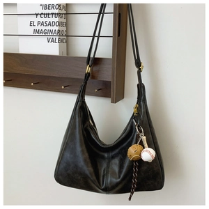 Detail of a black leather hobo bag with a retro oil-wax texture and a baseball charm