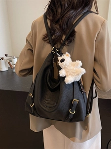 Black pebbled leather backpack with gold buckles and plush bear charm for commuting