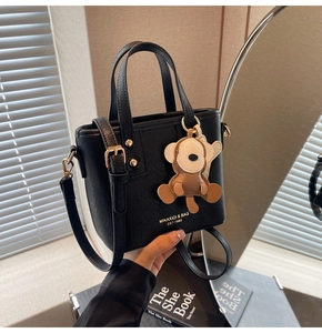 Nahaufnahme einer schwarzen Bucket Bag mit goldenem Logo, Metallschnalle und Affenanhänger
