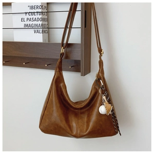 Brown leather hobo bag with sporty baseball charms shown in a lifestyle setting