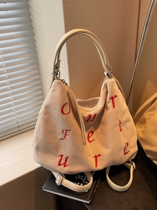Chic beige corduroy tote bag with red letter embroidery on a book by a window