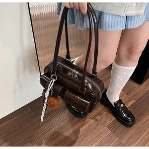 Détail d'un sac à bandoulière en cuir verni marron foncé avec pendentif et textures