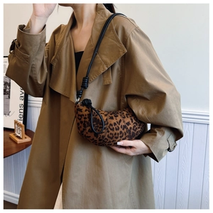 Detail shot of leopard print crescent bag with knotted rope strap worn with trench coat