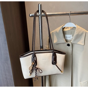Detail of off-white tote bag with dark brown trim and tennis racket charm accessory