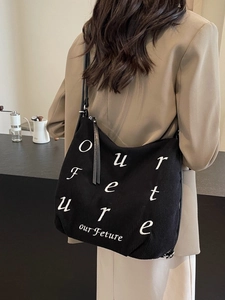 Minimalist black corduroy tote bag with white embroidery shown on a model's shoulder