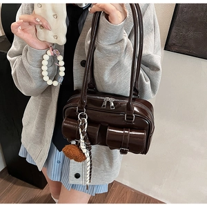 Détail d'un sac bandoulière en cuir verni marron foncé avec poches et charms