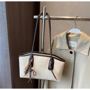 Detail of beige tote bag featuring brown leather trim and golden tennis racket charm