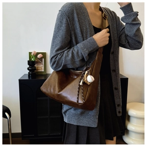 Detailed view of deep brown vintage leather crossbody bag with baseball charm on model