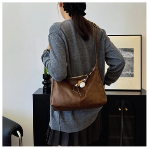 Detail view of large dark brown retro crossbody bag with baseball pendant accessory
