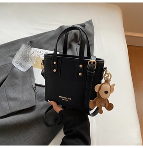 Detail der schwarzen Ledertasche mit goldenen Beschlägen und einem süßen Anhänger