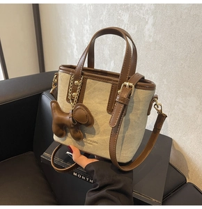 Detail of canvas bucket bag with brown leather trim, golden hardware and a dog charm