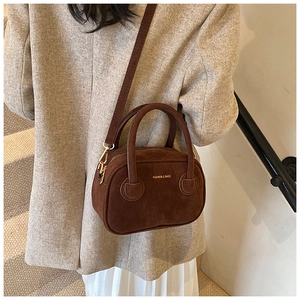 Détail d'un sac bandoulière en daim marron foncé porté avec un manteau beige élégant