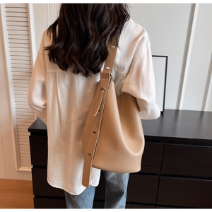 Detailed texture of khaki pebbled leather bucket bag worn by model in minimalist setting