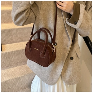 Détail d'un sac bowling en daim marron foncé avec ferrures dorées et lettrage fashion