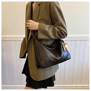 Detail of a dark brown hobo bag featuring vertical stitching and a baseball pendant