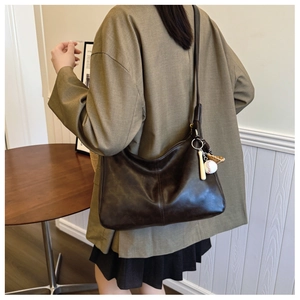 Detail of deep brown hobo bag with vintage leather texture and creative baseball pendant