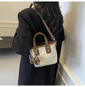 Detail of mini bucket bag with leather teddy bear charm and brown strap on black coat