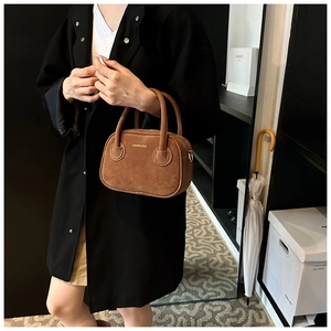 Gros plan du mini sac à main en daim marron avec logo doré et doubles poignées
