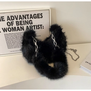 Détail du sac bandoulière en fausse fourrure noire avec chaîne argentée sur socle blanc