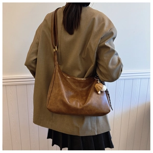 Brown retro hobo bag with plush mushroom charm worn by model against a white wall