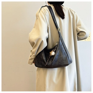 Detail of black leather crescent tote bag with baseball charm and gold buckle accents
