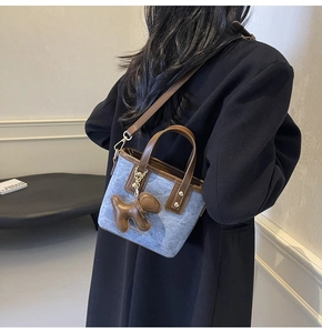 Detail of light blue denim mini tote bag with brown leather straps and puppy charm