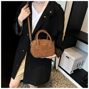 Détail d'un sac à main en daim marron foncé avec deux poignées et une bandoulière sur modèle