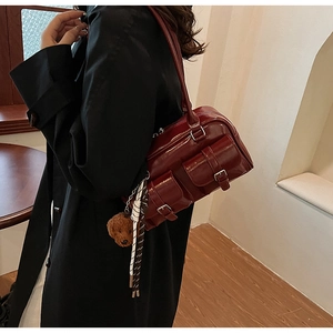 Gros plan d'un sac sous les bras en cuir verni bordeaux avec poches déco et charm d'ours en peluche