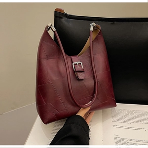 Close-up of a burgundy leather patchwork crescent bag with a silver buckle over vintage books