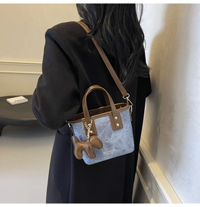 Detail of blue denim bucket bag with brown leather handles and a cute dog charm