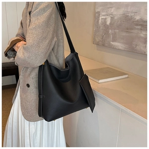 Side view of black pebble leather tote bag worn by model in a minimalist modern setting