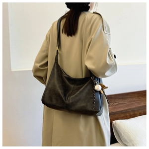 Detail of dark brown leather crossbody bag with wide strap and baseball charm