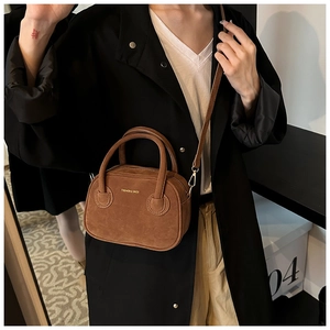 Sac bandoulière en suédine marron porté avec un trench noir pour un look chic au quotidien