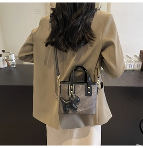 Model view of a grey bucket bag with black trim and a leather puppy charm detail