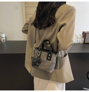 Detail of grey mini bucket bag featuring black leather trim and dog charm on a blazer