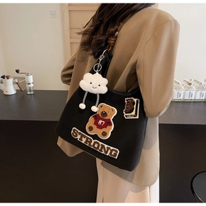 Dettaglio della borsa tote in tela nera con orsetto ricamato e patch in stile varsity
