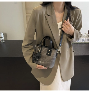 Detail of grey mini bucket bag with black leather handles and cute dog charm accessory