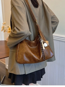 Brown faux leather crossbody bag with stylish baseball charm shown on model in a suit