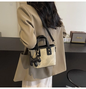 Detail of a contrast color bucket bag with black dog pendant shown on a brown blazer outfit