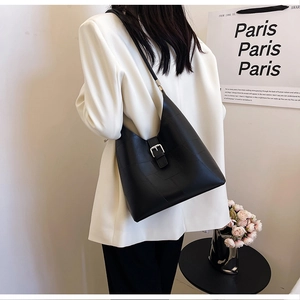 Model wearing a black shoulder tote bag with geometric stitching and silver buckle