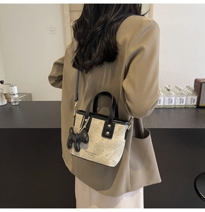 Detail of crossbody bucket bag with beige marble pattern and black puppy charm accessory