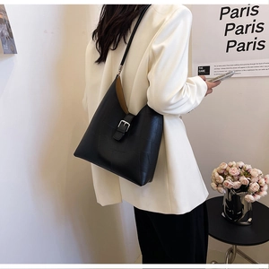 Close-up of black PU leather shoulder bag with buckle strap on model in urban setting