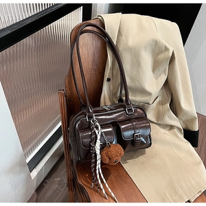 Détail d'un sac d'épaule en cuir marron brillant avec poches et breloque ours