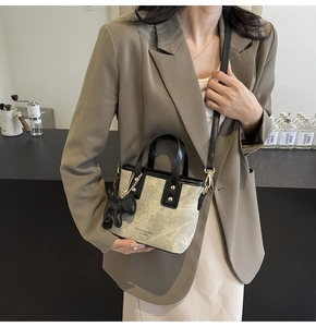 Detail of beige tote bag with black handles, gold hardware, and a small dog charm