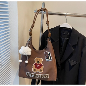 Dettaglio della borsa marrone Maillard con ricamo orso e ciondolo nuvola sul blazer