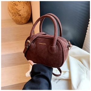 Détail d'un sac bowling en daim marron foncé avec ferrures dorées et lettrage chic